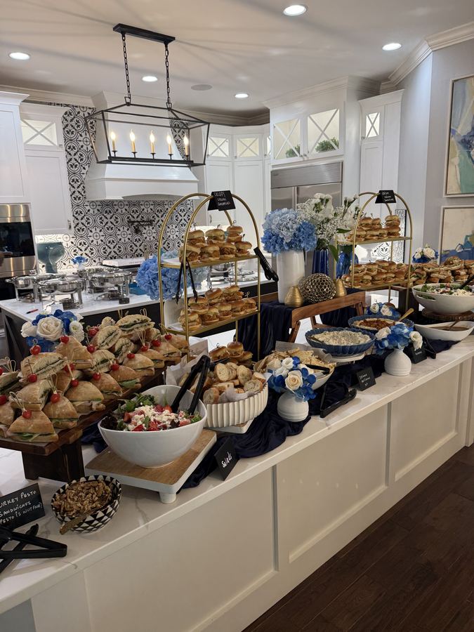 A long grazing counter with gold tier stands of sliders, sandwiches, salads and blue hydrangeas